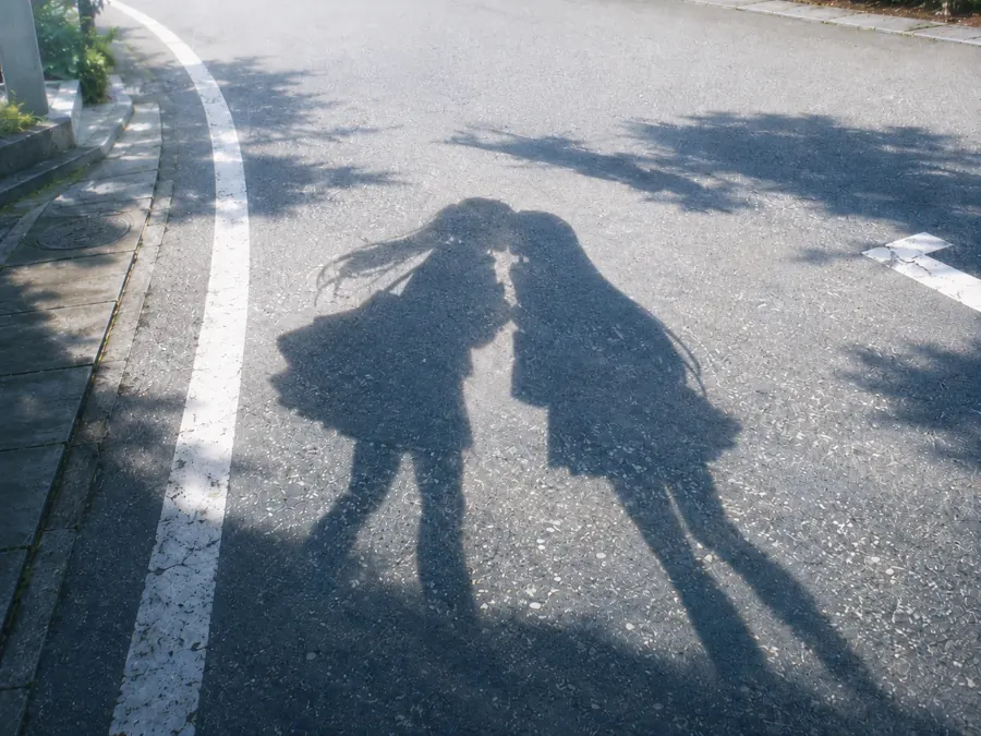 柏油路上两个女孩靠在一起的影子